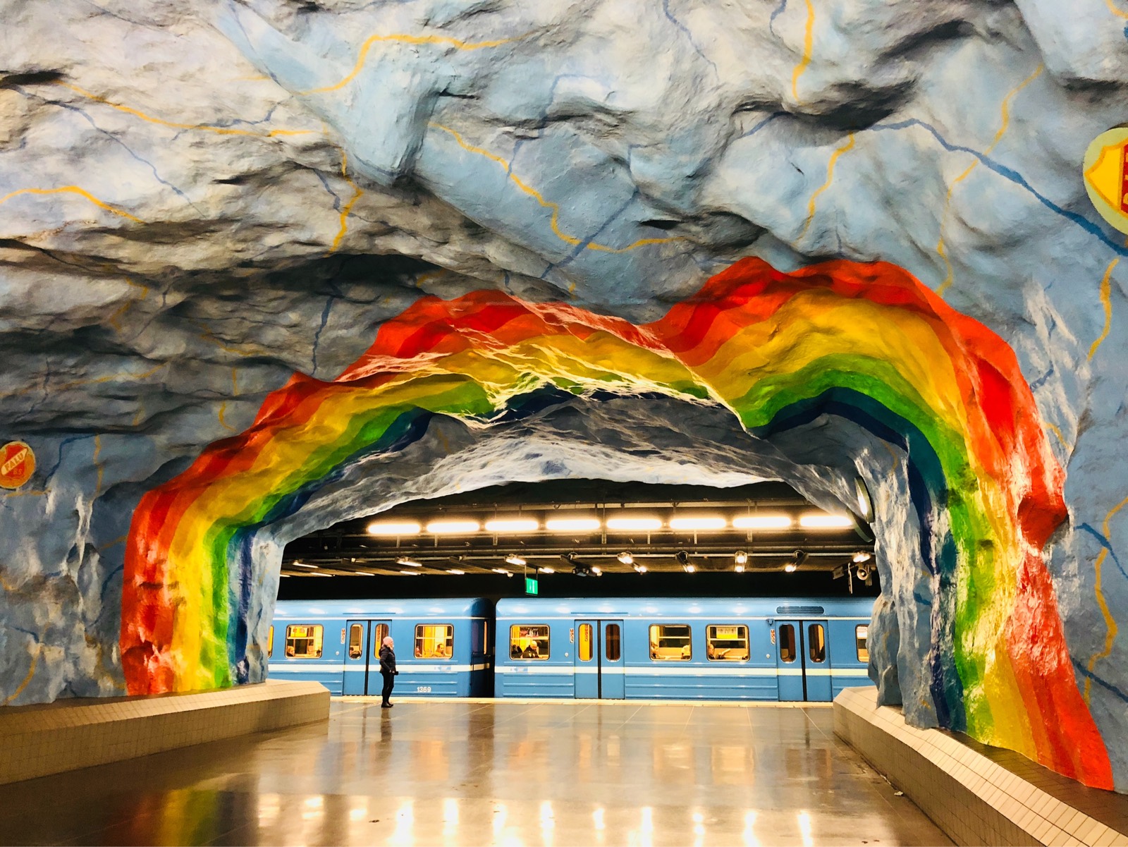 U-Bahnstation mit Regenbogendecke und hellblauem Zug im Hintergrund