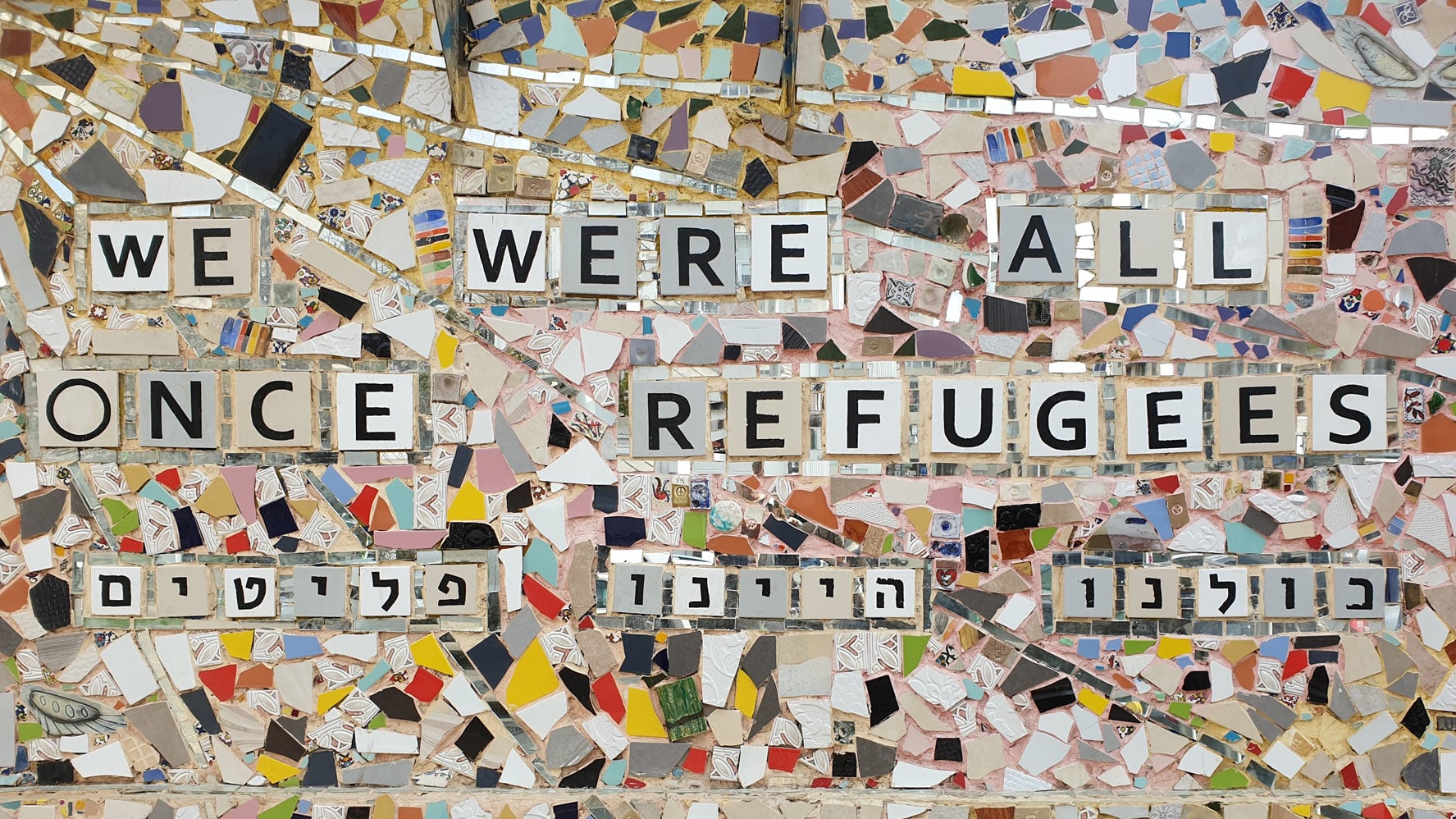 Mosaiksteine auf einer Wand mit der Aufschrift We Were All Once Refugees.