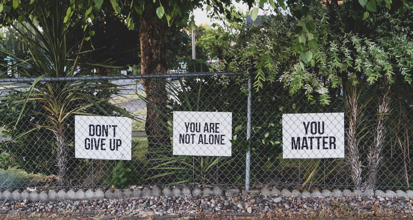 3 Schilder hinter einem Zaun mit den Aufschriften: Don't Give Up. You're not alone und You Matter.
