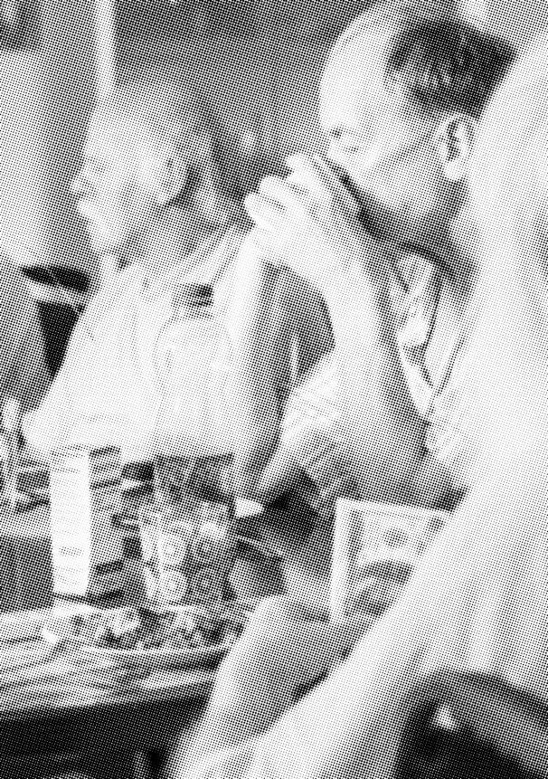 Schwarz-Weiß-Fotografie von 2 Personen am Tisch sitzend. Eine Person trinkt aus einem Becher.
