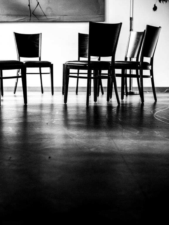 Schwarz-Weiß-Fotografie von mehreren Stühlen, die im Kreis stehen.